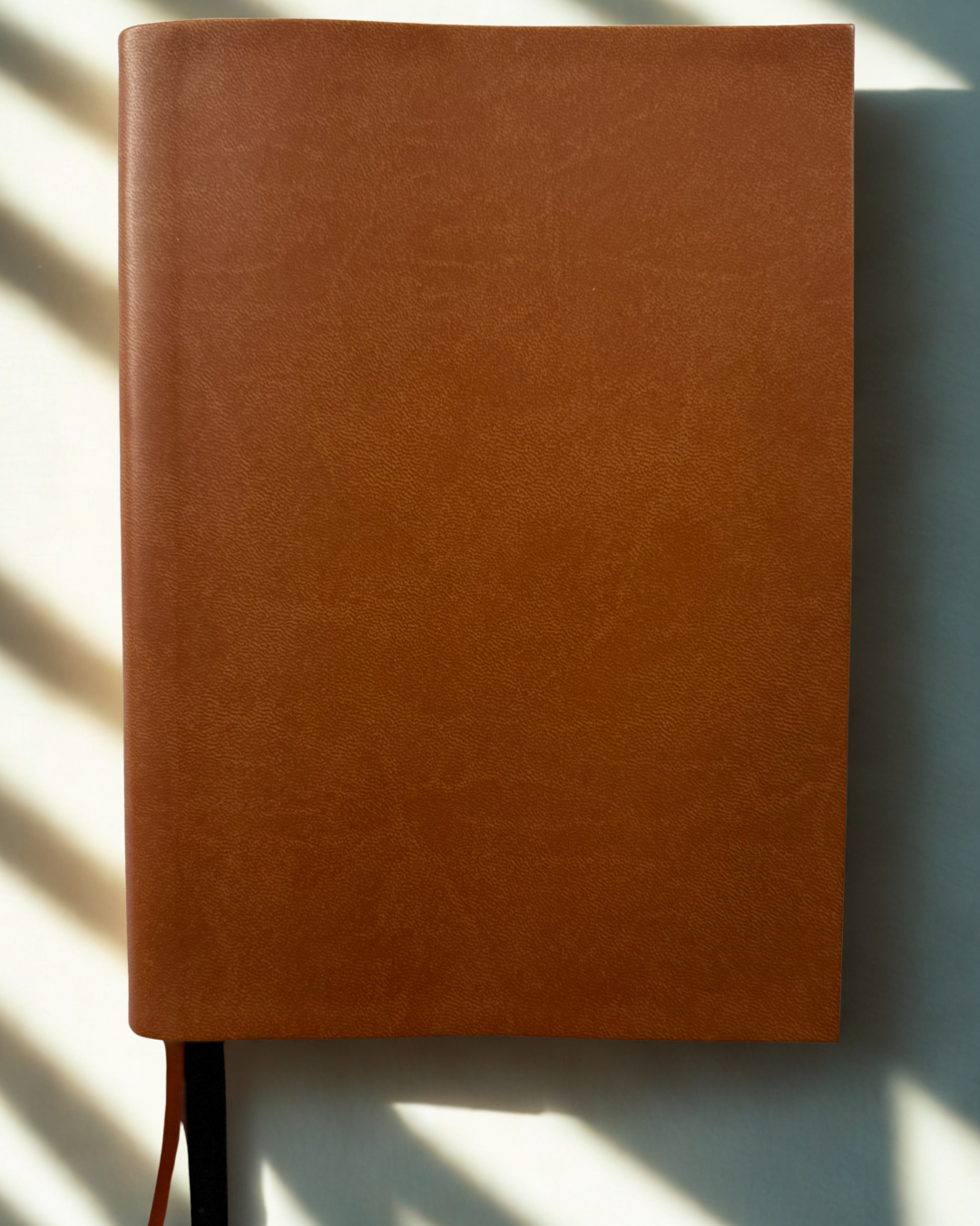 Brown leather notebook on a light surface with shadows